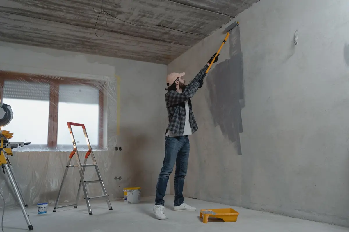 A painter rolling grey paint onto a wall.
