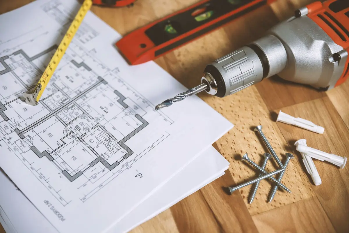 A floor plan, tape measure and drill on a workbench.