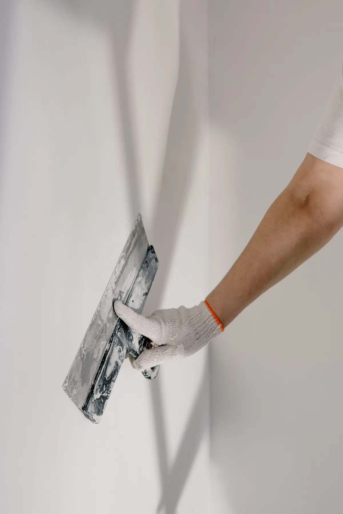 A gloved hand holding a plastering trowel to a wall.