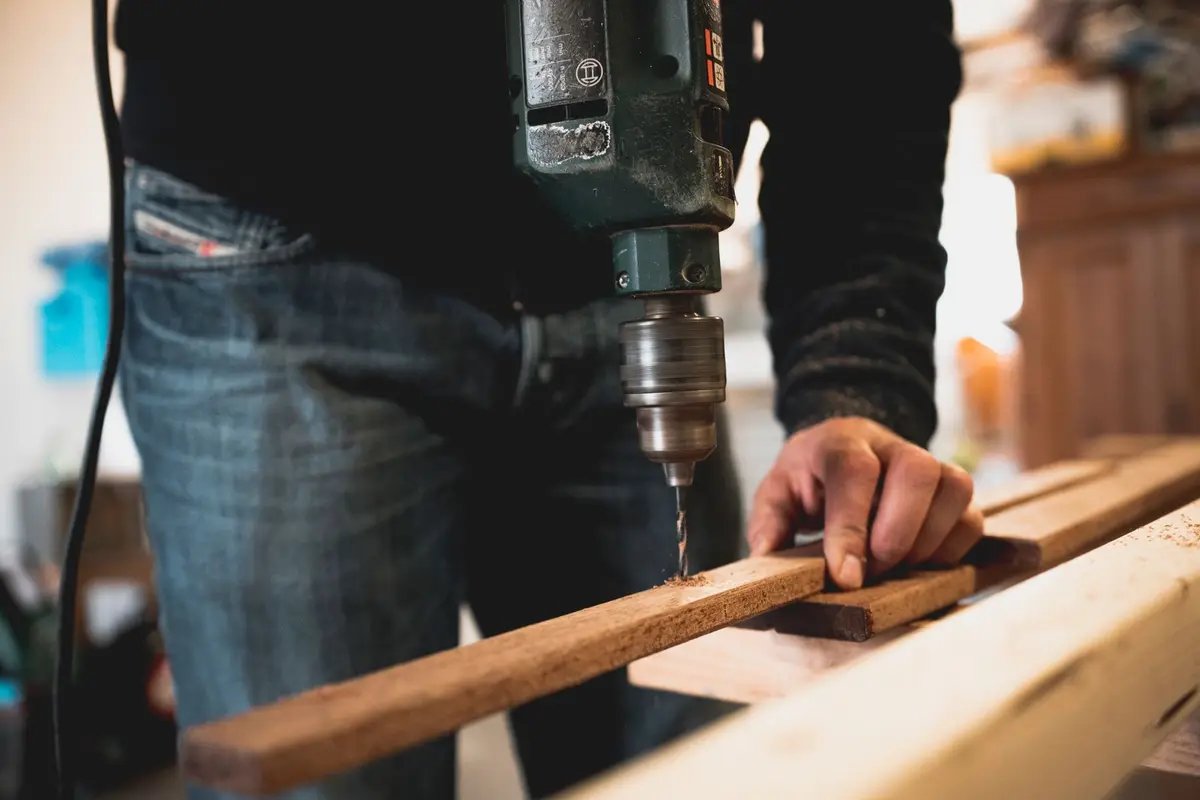 Hands drilling a wooden board.