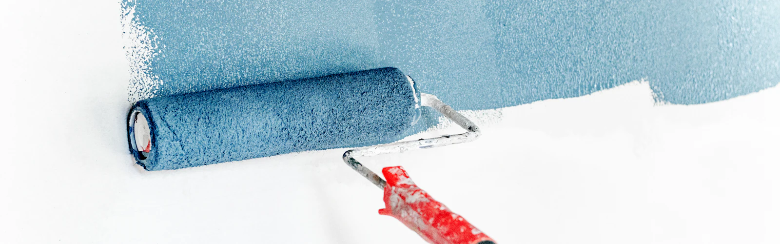 Paint roller applying blue paint to a white wall